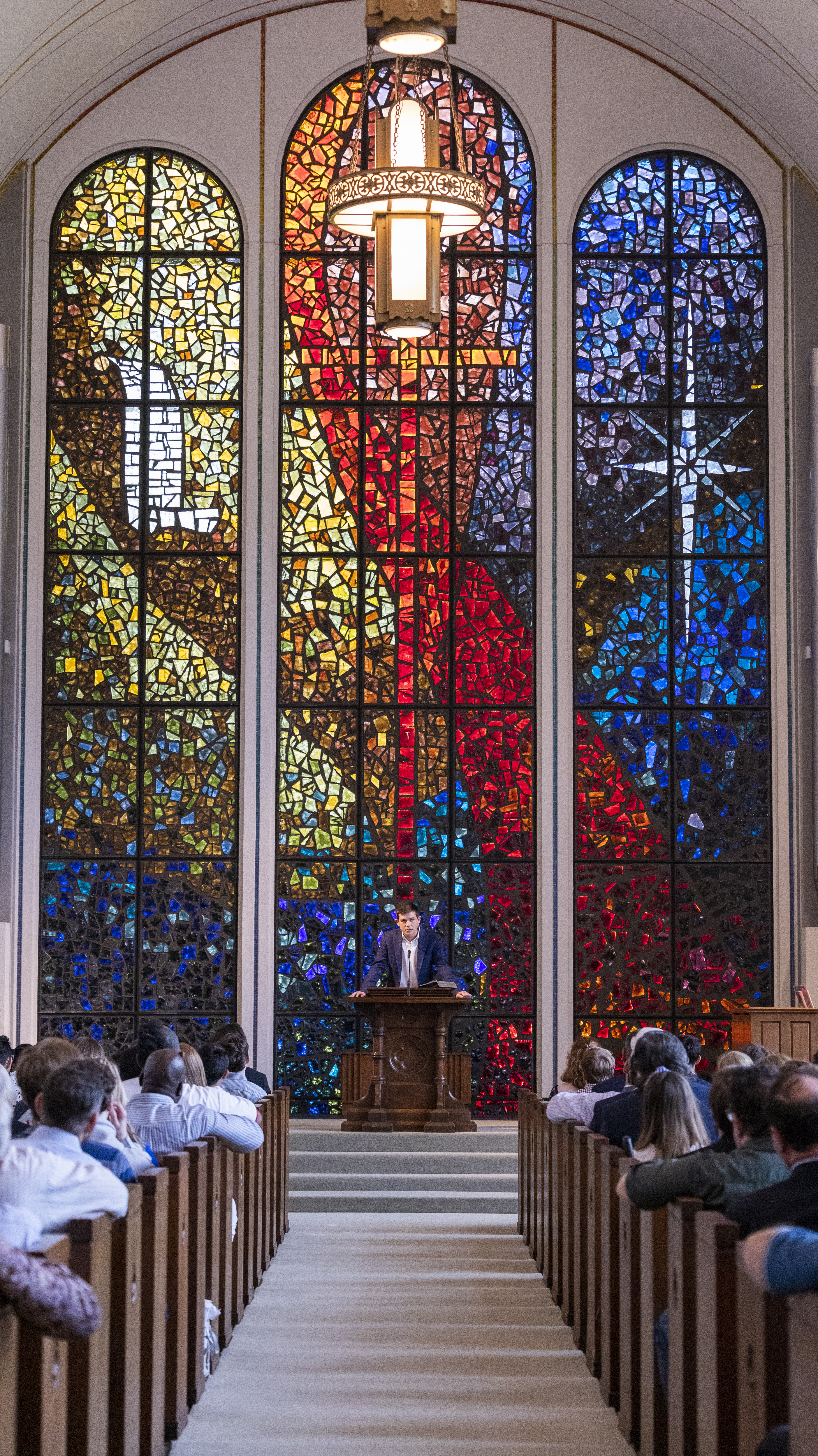 stained glass window with a youth preaching from the pulpit in front