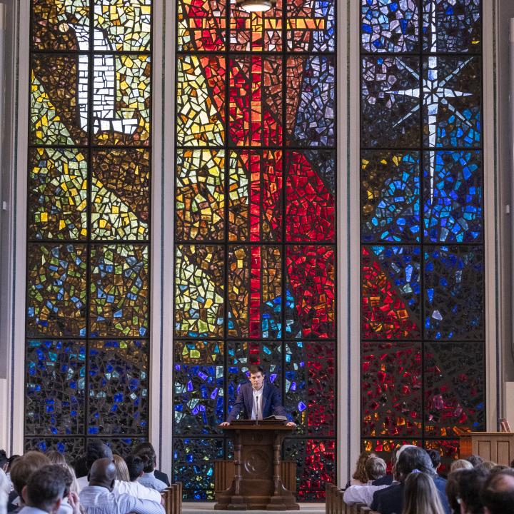 stained glass window with a youth preaching from the pulpit in front